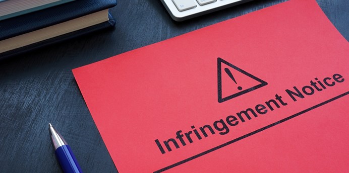 A red folder on a desk with the words "Infringement Notice" on the front