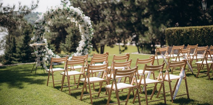 An outdoor wedding ceremony set up with a decorative arch, empty chairs and flowers