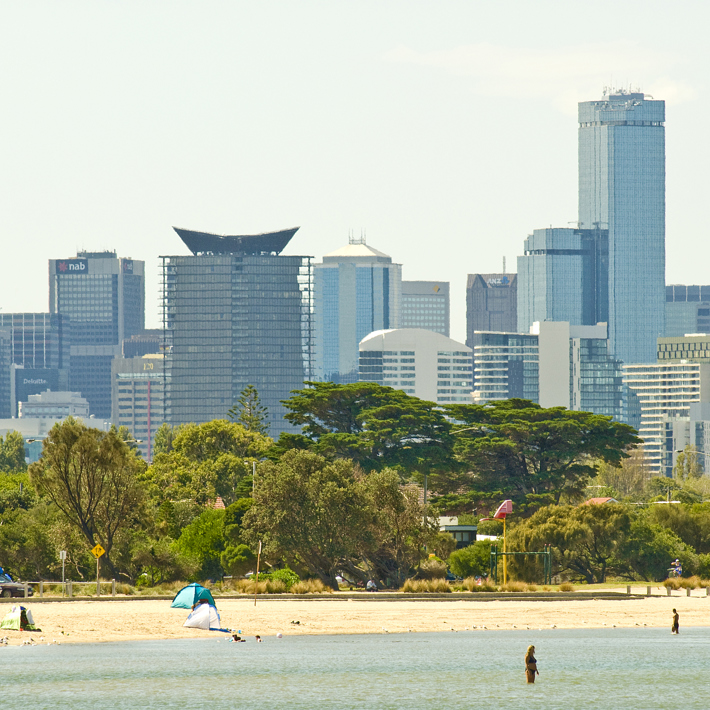 People in the water and enjoying Sandridge Beach with the City skyline in the distance 