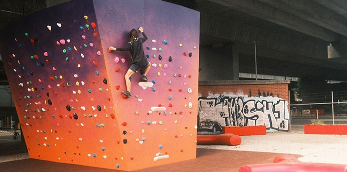 Young person climbing a bouldering wall attached to an elevated roadway in Fishermans Bend