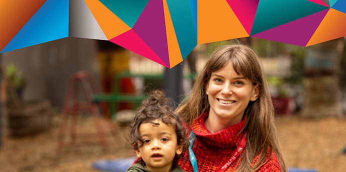 Smiling educator in a childcare centre holds a toddler on their knee