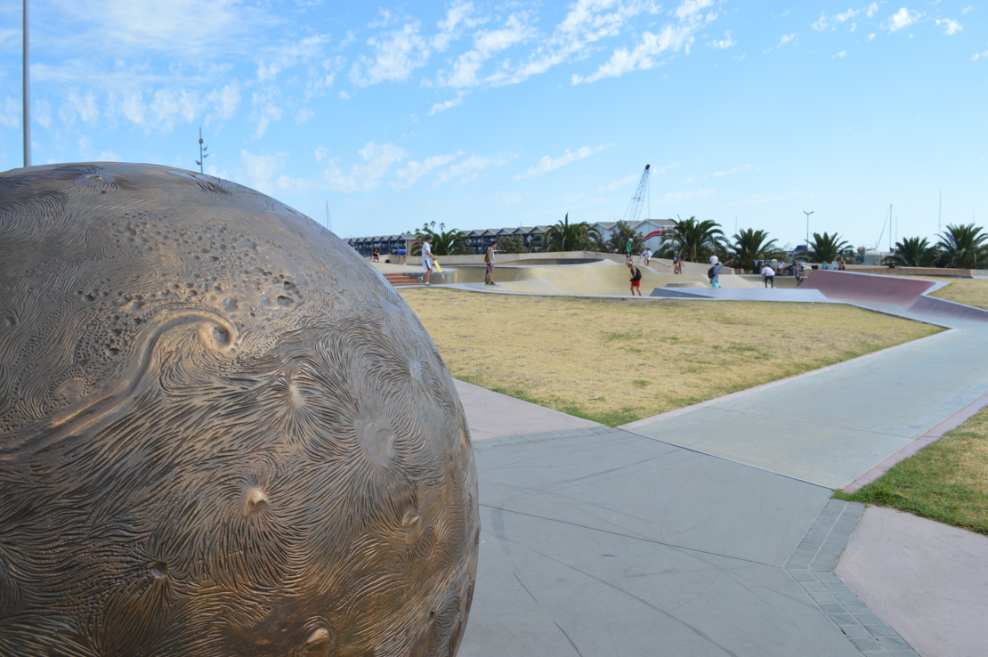 Skaters using the Marina Skate Park with the boat sheds in the background. Wide paved footpaths provide easy access.  