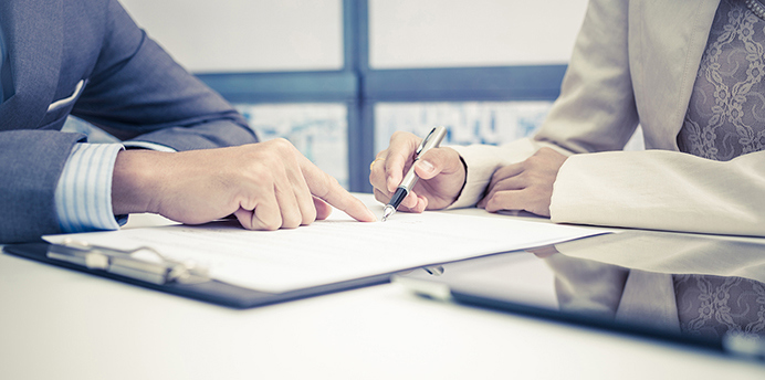 Two people reviewing and signing documents at a desk in a modern office
