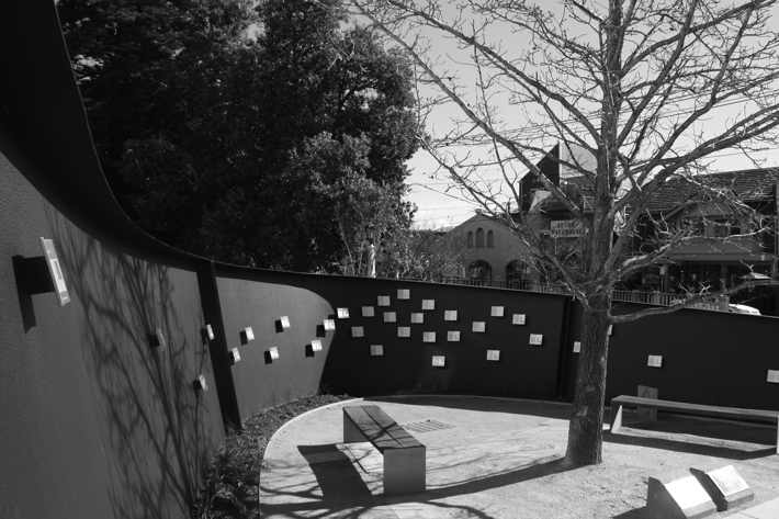 View of the curved wall that encompasses a garden and seating, metal schutz passesalso visible attached to the wall.