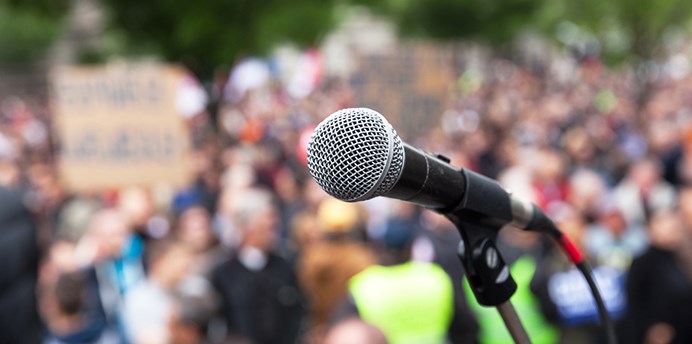 A microphone on a stand in front of a blurred crowd of protestors