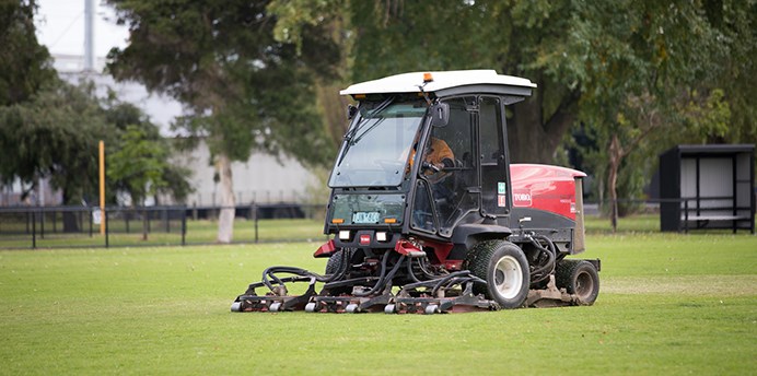 A specialised ride-on lawn maintenance vehicle being driven on a sporting ground