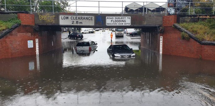 Cars partially submerged in flood waters under a train bridge