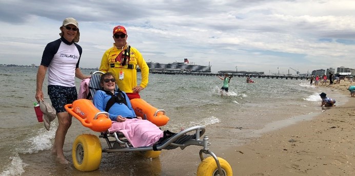 Person with a disability in a beach wheelchair accompanied by life saver