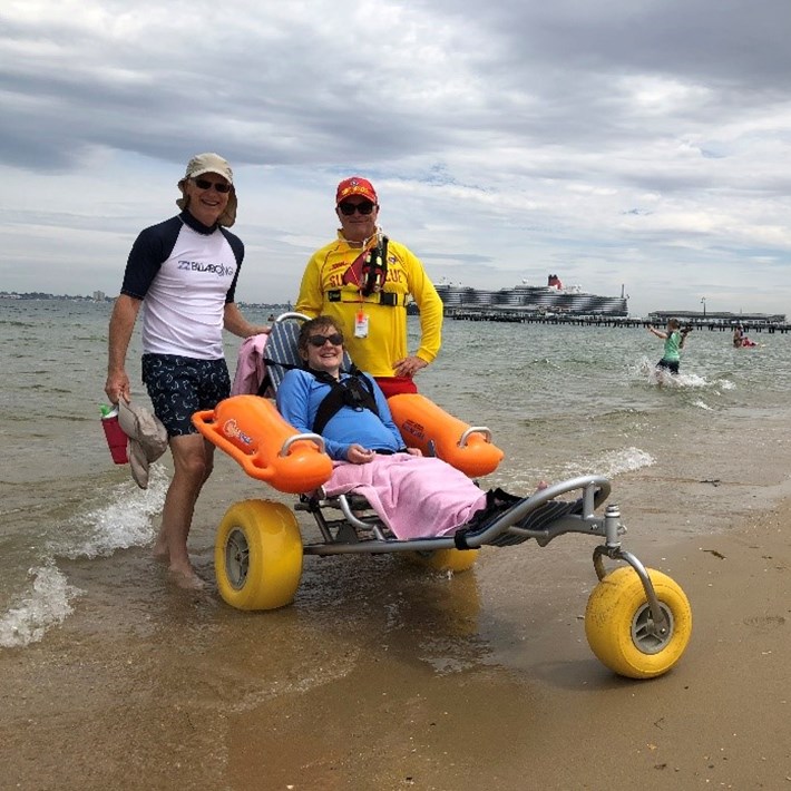Person with a disability in a beach wheelchair accompanied by life saver