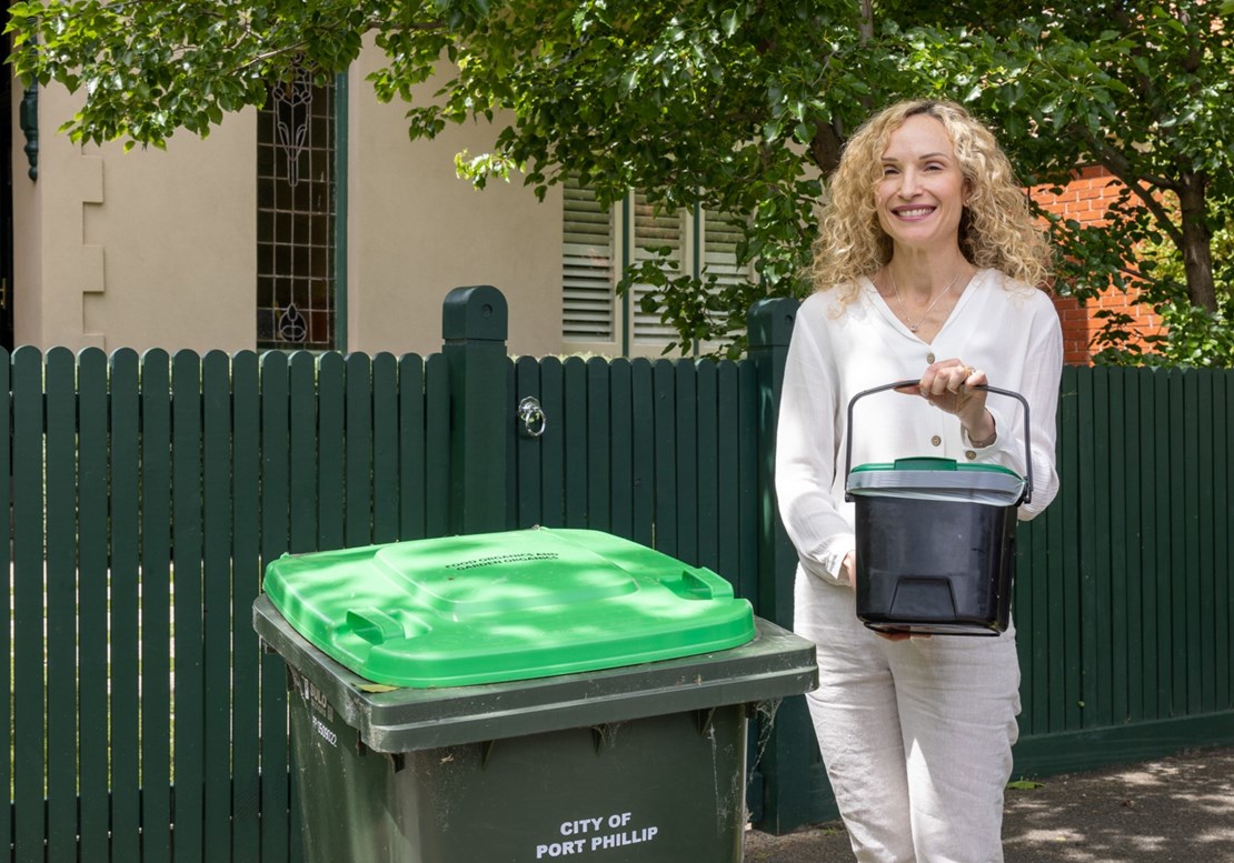 A woman stands next to a FOGO bin, she's holding a kitchen caddy 