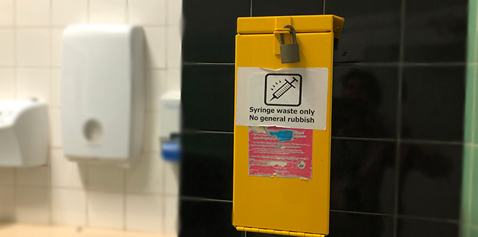 Yellow sharps bin in a public toilet for safe disposal of syringes