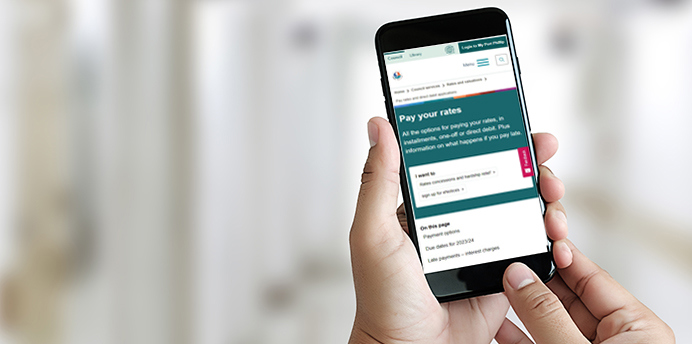 A person's hand holding a smartphone with the web page for paying rates on the screen